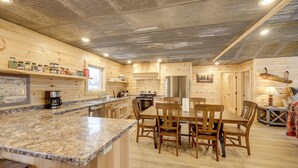 A kitchen with wooden cabinets, granite countertops, and a dining area with wooden chairs and a table. - New-Build, Mtn-View White Sulphur Springs Home! (White Sulphur Springs)