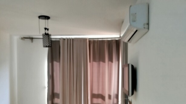 A room with a sofa, a TV mounted on the wall, a window with curtains, and a ceiling fan. - Spacious 3-bedroom apartment in phenomenal Alexandria Governorate with AC (Alexandria Governorate)