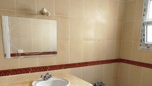 A bathroom with beige tiles, a white sink, a mirror, and a bathtub. - Spacious 3-bedroom apartment in phenomenal Alexandria Governorate with AC (Alexandria Governorate)
