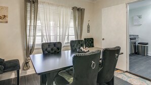 Una zona de menjador amb taula i caires a conjunt, una finestra amb cortines lleugeres i vista a la cuina.