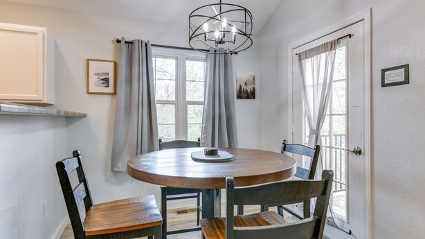 A dining area with a round table, four chairs, a chandelier, and two windows with curtains. - Mtn Views & Hot Tub: Modern Gatlinburg Townhome (Gatlinburg)