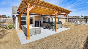 Ein überdachter Patio-Bereich mit einer Holzpergola, Gartenmöbeln und einem Grill.