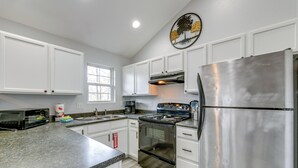 Una cocina con armarios blancos, electrodomésticos de acero inoxidable, encimera de granito y una ventana.