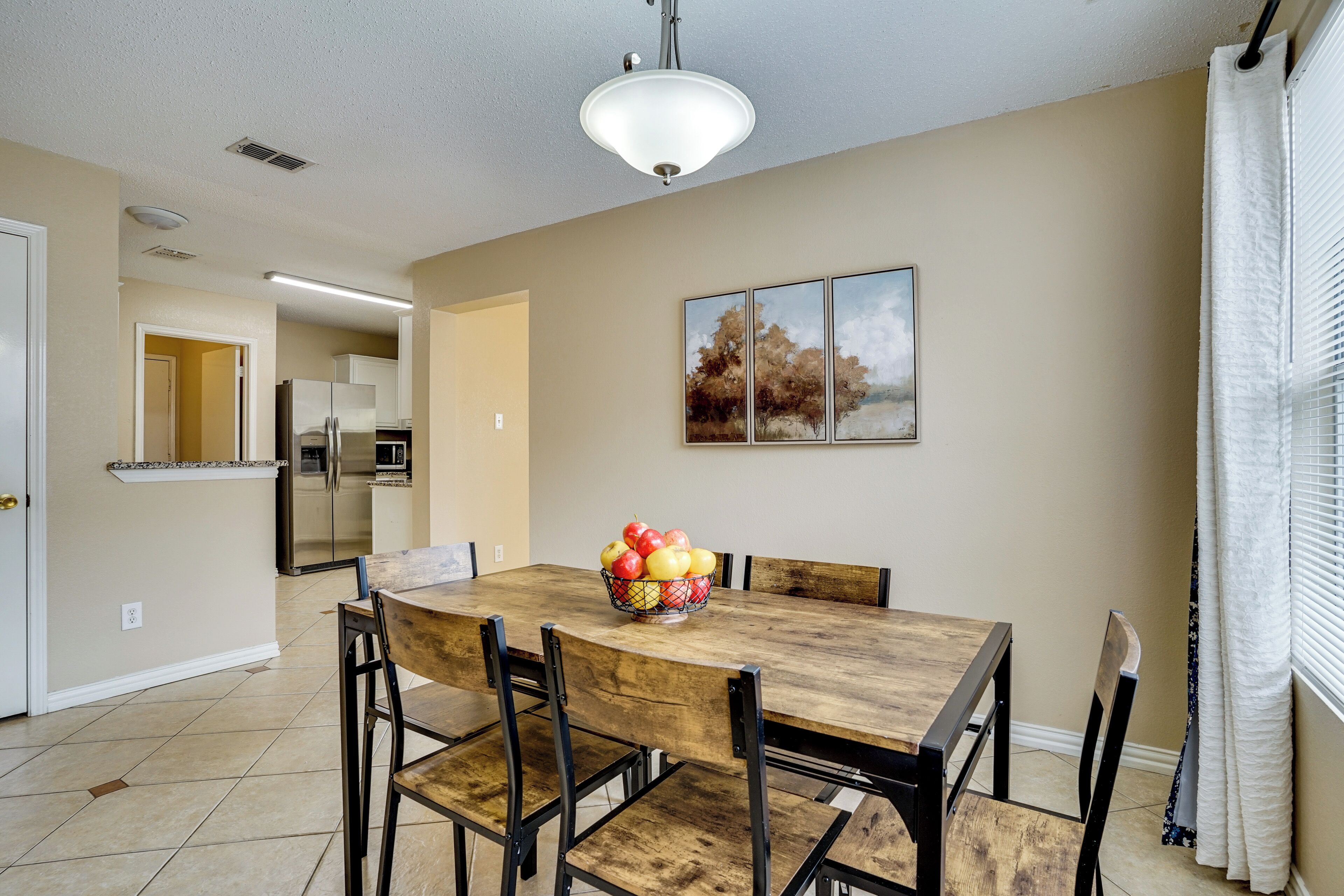 A dining area with a wooden table and chairs, a fruit bowl, and a painting on the wall.