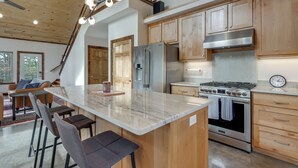 A modern kitchen with a central island, stainless steel appliances, wooden cabinets, and a visible clock. - Epic Lake Views! 'The Ridge' Eureka Springs Home (Eureka Springs)