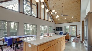 A spacious kitchen with wooden cabinets, a large island, and a dining area with a table and chairs. There are large windows providing natural light and views of the outdoors. - Epic Lake Views! 'The Ridge' Eureka Springs Home (Eureka Springs)