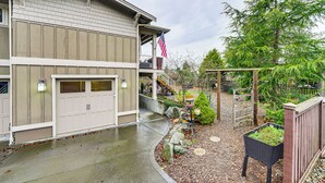 A two-story house with a garage, a covered porch, and a small garden area with plants and a wooden fence. - Near Ferry, Shops & Eats! Anacortes Townhome (Anacortes)