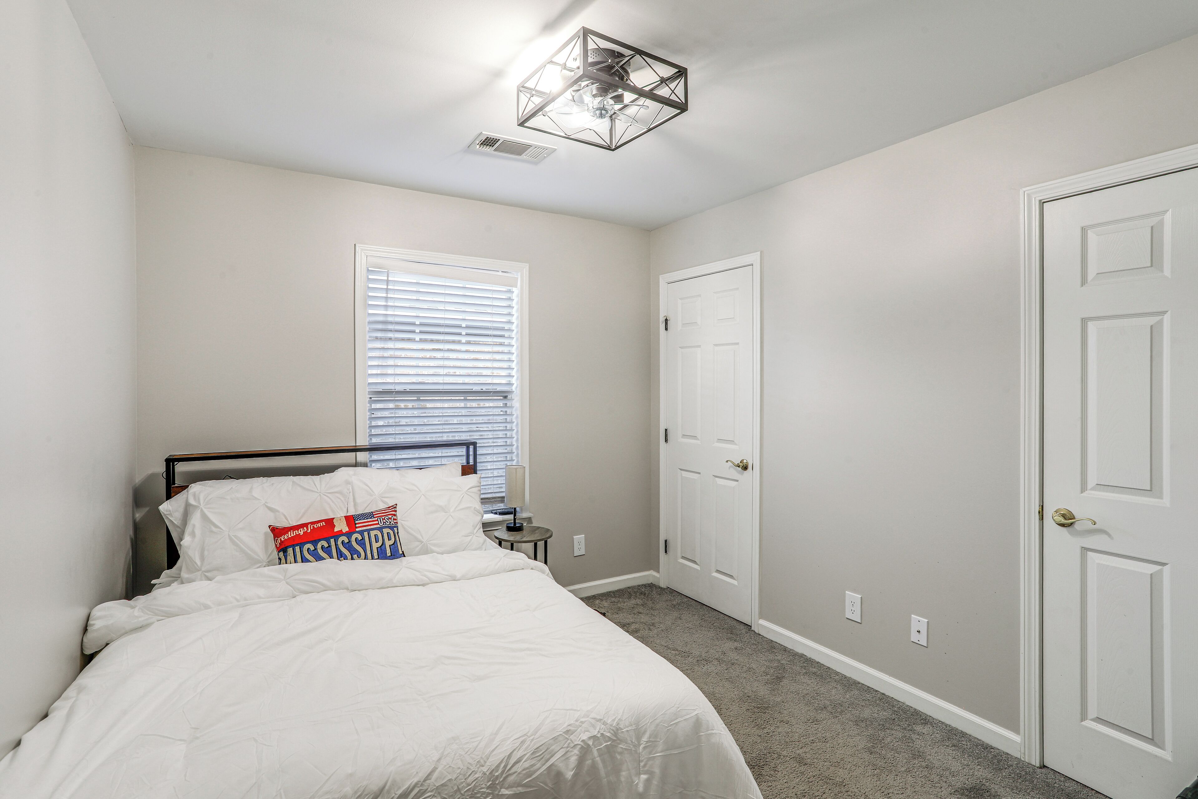 A bedroom with a bed, a window with blinds, a door, and a ceiling light fixture.