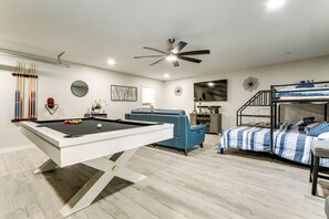 A modern living room with a pool table, a blue sofa, a bunk bed, and a ceiling fan. - Sand Volleyball Court, Pool, Hot Tub! Fun Retreat (Savannah)
