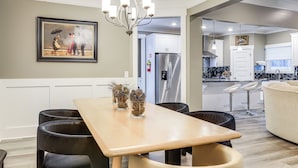 Una cocina moderna con un refrigerador de acero inoxidable, un comedor con mesa de madera y sillas negras, y un cuadro en la pared.