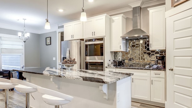 Una cocina moderna con muebles blancos, electrodomésticos de acero inoxidable, una isla de mármol con taburetes y luminarias colgantes.