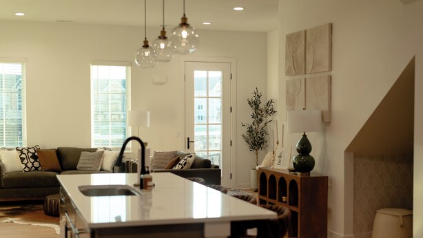 Cocina moderna con una isla central, comedor y sala de estar con sofá y cojines decorativos.