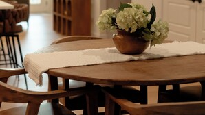 Un comedor con mesa y sillas de madera, un florero con flores y una puerta blanca al fondo.