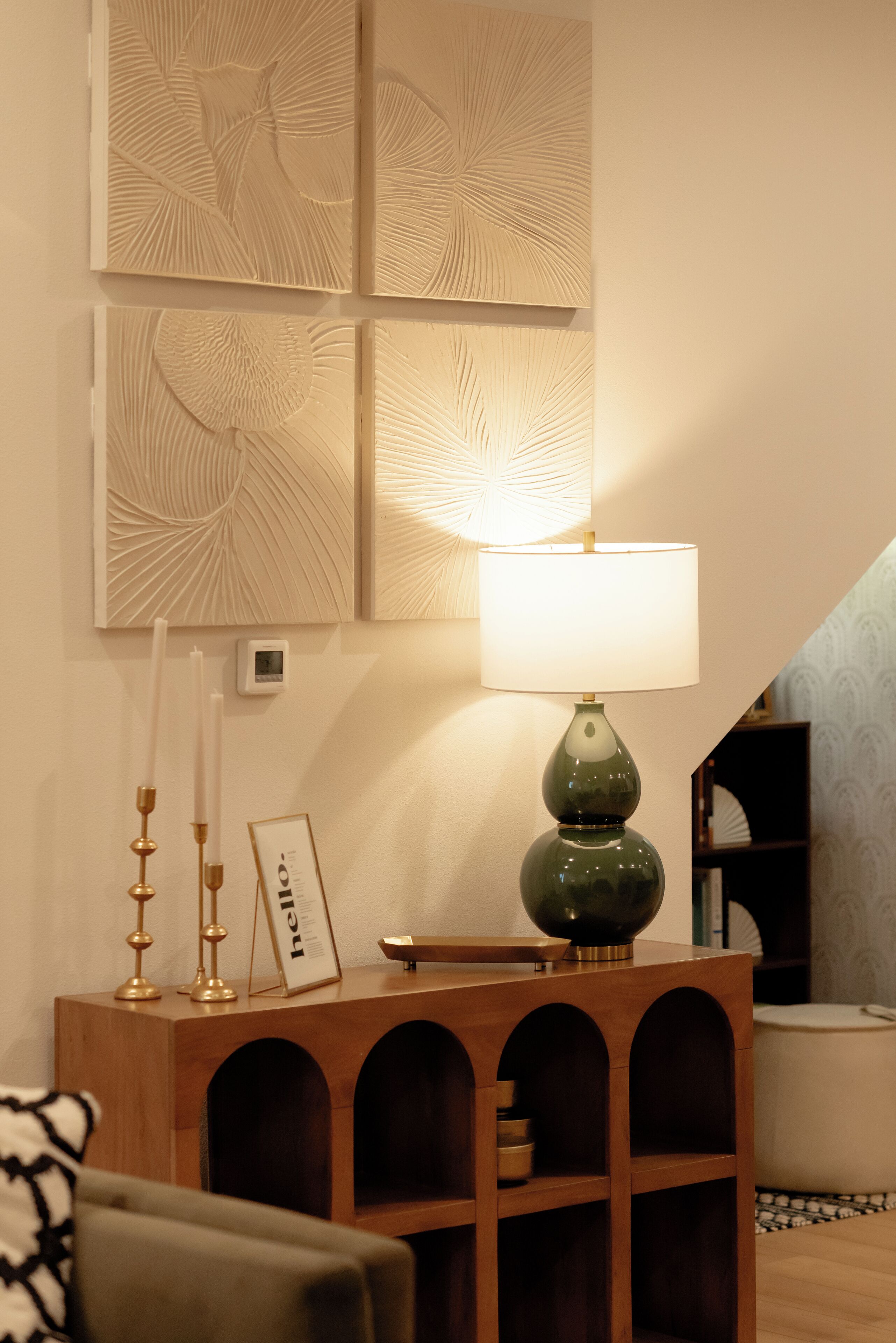 A neatly arranged room with a wooden console table, a green lamp, and wall art.
