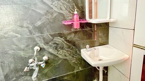 Een badkamer met een marmeren vloer, een witte wastafel, een spiegel en een roze zeepdispenser.