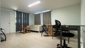 Una habitación amplia con sofá, una mesita, un escritorio con silla y una puerta.