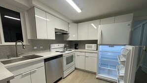 Una cocina moderna con armarios blancos, un lavaplatos de acero inoxidable, un microondas integrado y un refrigerador con congelador.