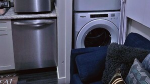 A compact living space with a built-in washer and dryer, a stainless steel refrigerator, and a blue sofa with decorative pillows. - MegaVille: Serene, peaceful and relaxing apartment while working or on vacation. (Saskatoon)