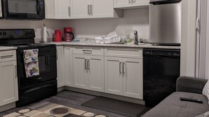 A modern kitchen with white cabinets, a black microwave, a stainless steel refrigerator, a dishwasher, and a gray sofa with a remote control on it. - MegaVille: Serene, peaceful and relaxing apartment while working or on vacation. (Saskatoon)