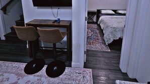 A compact living space with a TV mounted on the wall, a small dining area with two chairs, a bed with a floral bedspread, and a staircase leading to another level. - MegaVille: Serene, peaceful and relaxing apartment while working or on vacation. (Saskatoon)