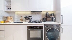 A modern kitchen with white cabinetry, a built-in oven, a microwave, and a dishwasher. - Modern Studio in Binghatti Azure WPool & Gym (Dubai)
