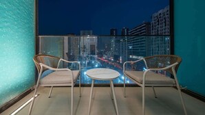 A balcony with two wicker chairs and a small round table, overlooking a cityscape at night. - Modern Studio in Binghatti Azure WPool & Gym (Dubai)