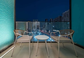 Ein Balkon mit zwei Korbstühlen und einem kleinen runden Tisch, mit Blick auf eine nächtliche Stadtansicht.