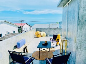 A rooftop terrace with a table and chairs, a yellow umbrella, and a view of the sea.