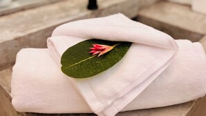 A bathroom with a white towel folded on a stone surface, a green leaf, and a black faucet.
