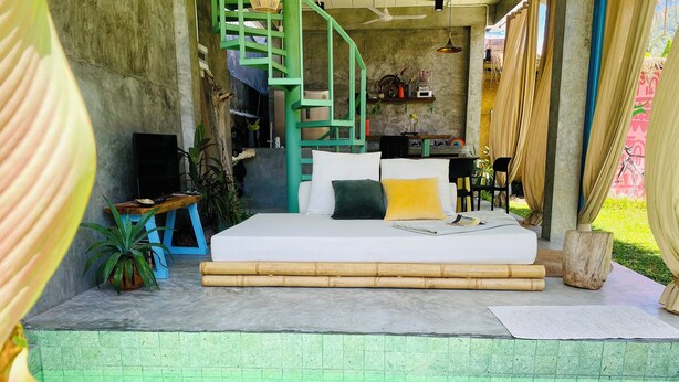 A bedroom with a green staircase, a bed with white bedding, and a small table with a plant.