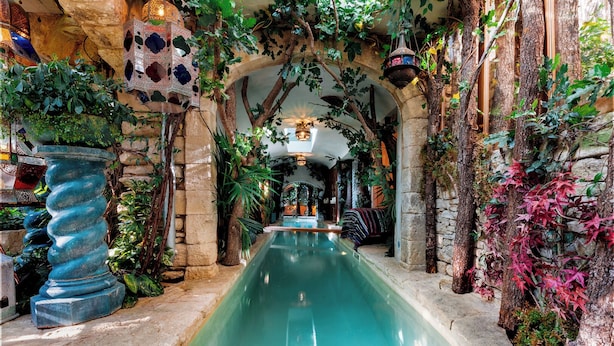 An indoor pool with stone walls and arches, surrounded by lush greenery and hanging plants. - The Pool House - Organic Charm & Pool (Goult)