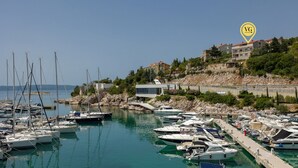 A marina with various boats docked, a building labeled 'Mitan Marina', and a hillside with residential buildings. - Apartman Vesna beachfront by Villas Guide (Novi Vinodolski)