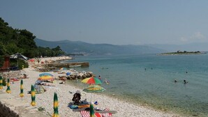 A beach with umbrellas, people swimming, and a clear view of the sea and distant mountains. - Apartman Vesna beachfront by Villas Guide (Novi Vinodolski)