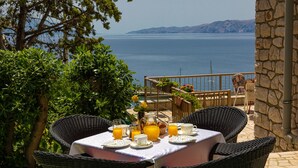 A table set for breakfast with orange juice, a pitcher, and a cup, overlooking a scenic view of the sea and mountains. - Apartman Vesna beachfront by Villas Guide (Novi Vinodolski)