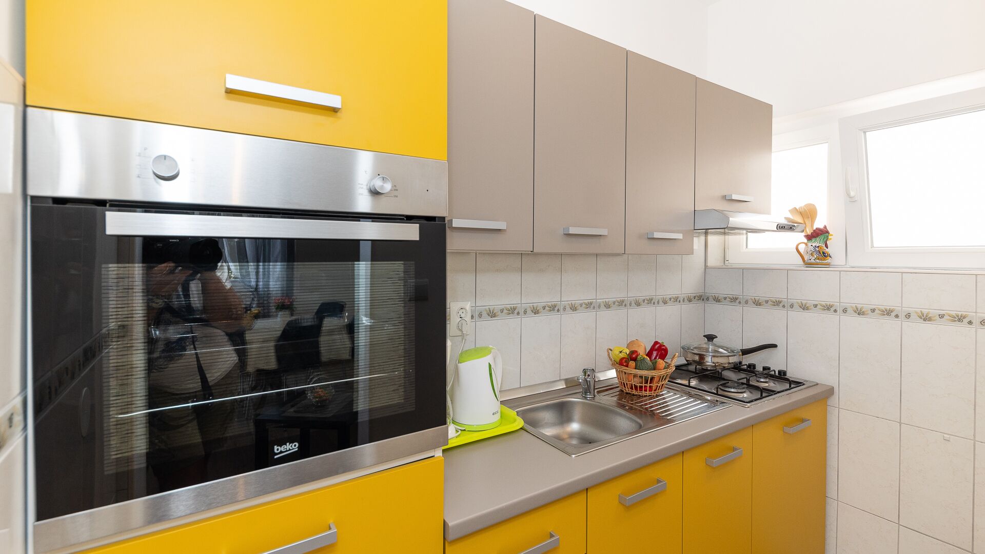 A kitchen with yellow cabinets, a stainless steel oven, a sink, and a window above the counter.