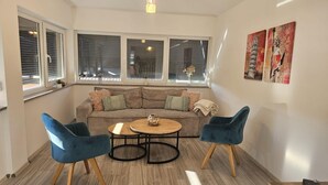 A cozy living room with a sectional sofa, two blue armchairs, a coffee table, and a view through large windows with blinds. - Apartman Damir 1 by Villas Guide (Galižana)