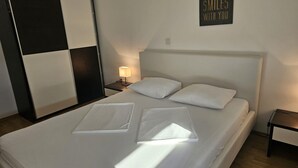 A neatly made bed with white linens and pillows, a bedside table with a lamp, and a wall sign saying "SMILES WITH YOU". - Apartman Damir 1 by Villas Guide (Galižana)