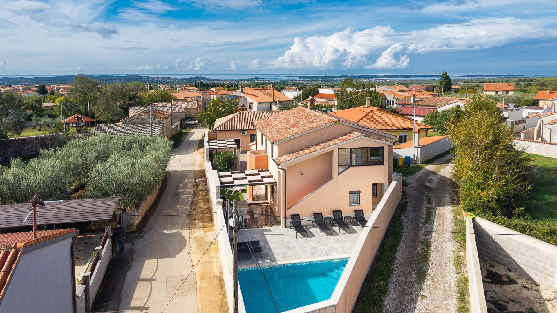 A residential area with a swimming pool, terracotta-roofed houses, and a clear view of the surrounding landscape.