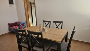 A dining area with a wooden table and four chairs. There is a small decorative item on the table, and a sofa with a colorful blanket in the background. - Apartman Damir 1 by Villas Guide (Galižana)