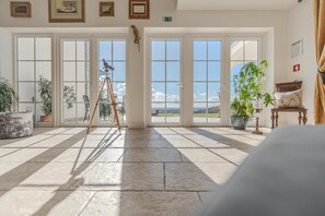 A spacious room with large windows, a ladder, and potted plants.