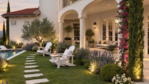 Una casa de dos pisos con un porche cubierto, mobiliario exterior y una piscina.