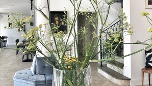 Una sala de estar moderna con un florero grande de vidrio con flores amarillas sobre una mesa de centro, un sofá azul y una escalera al fondo.