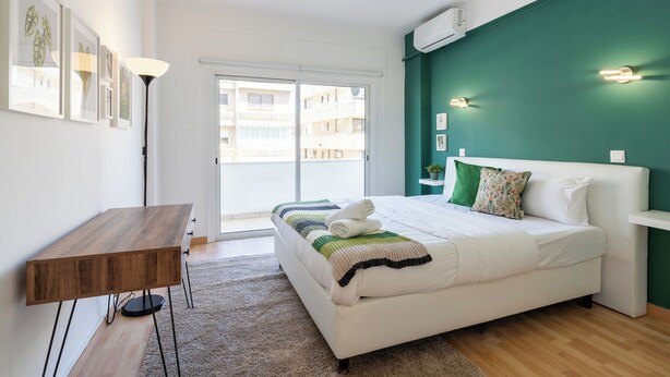 A modern bedroom with a bed, a desk, and a view of the outside. - Oracle 2-BR Apt. & Balcony in Larnaca (Larnaca)