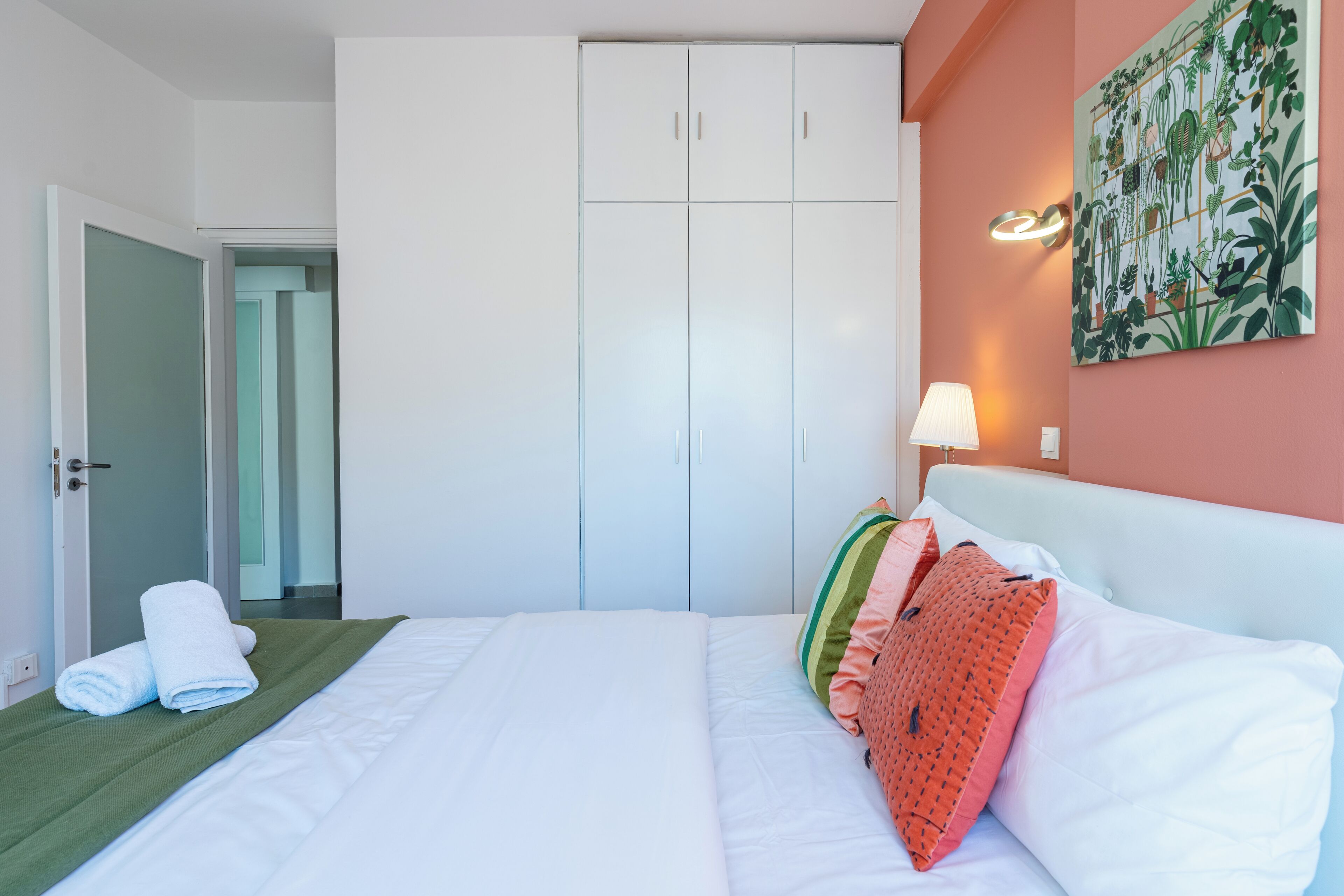 Una camera d'albergo con un letto, un armadio, un tappeto verde e un quadro con una pianta.