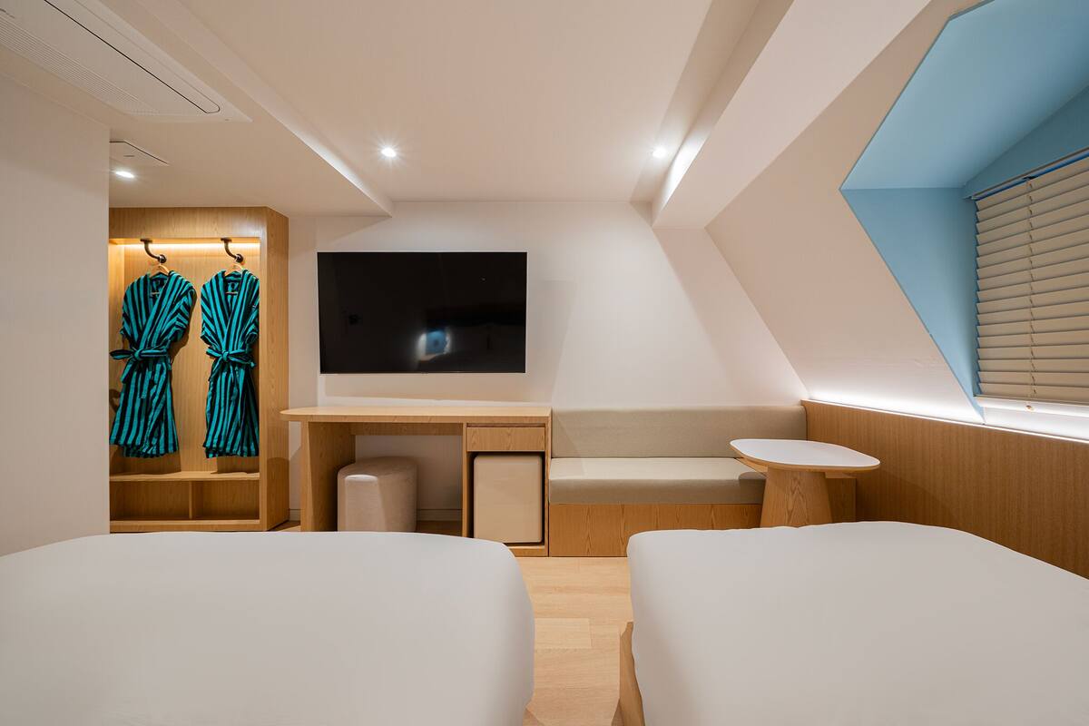 A modern hotel room with a flat-screen TV, a desk, two beds, a small table, and a seating area.