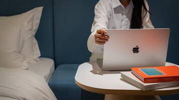 Een persoon zit op een blauwe bank met een laptop en boeken op een ronde tafel.