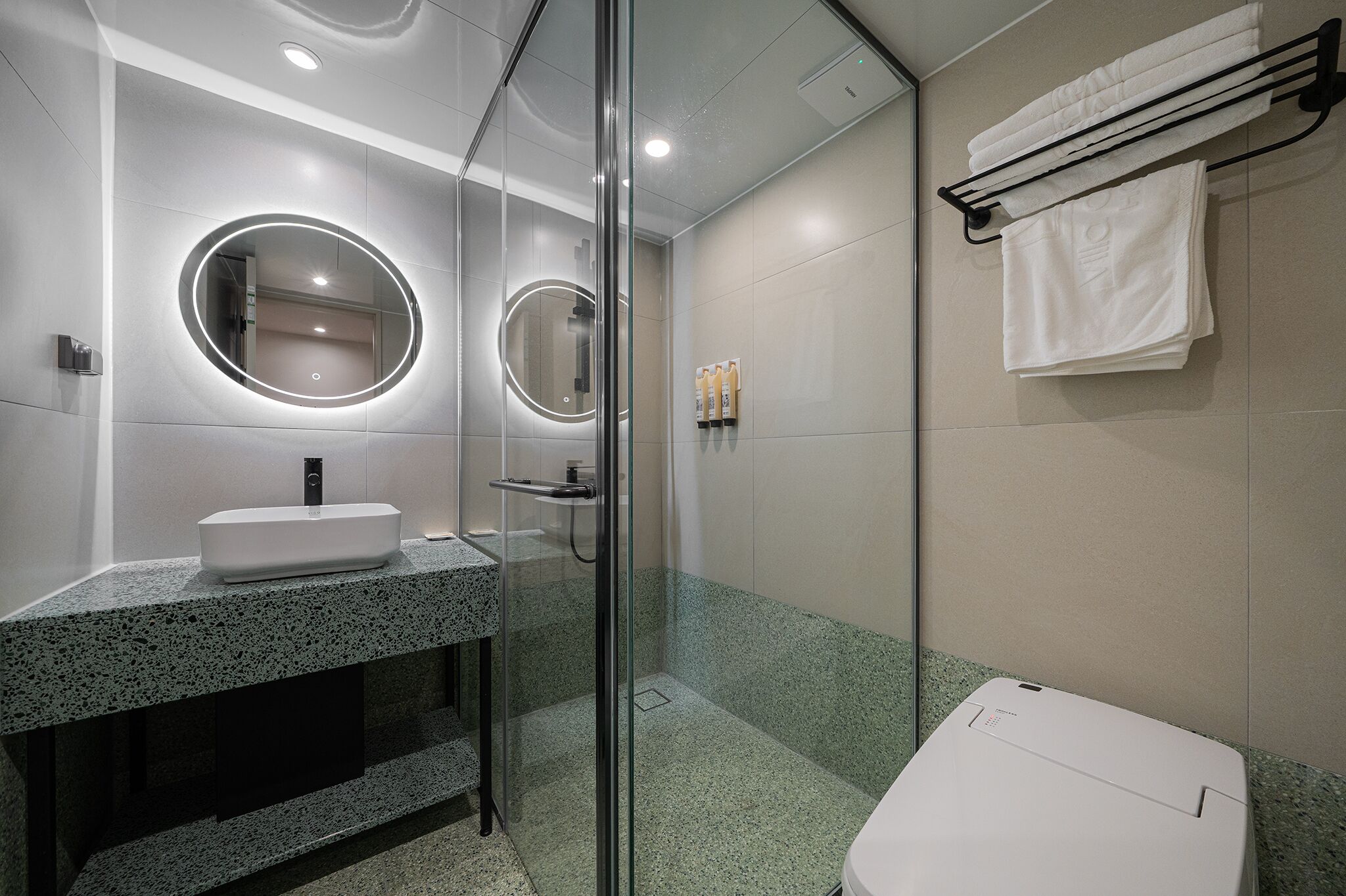 Une salle de bain moderne dotée d’une douche à parois de verre, d’un lavabo surmonté d’un plan de travail en granit et d’un porte-serviettes avec des serviettes pliées.