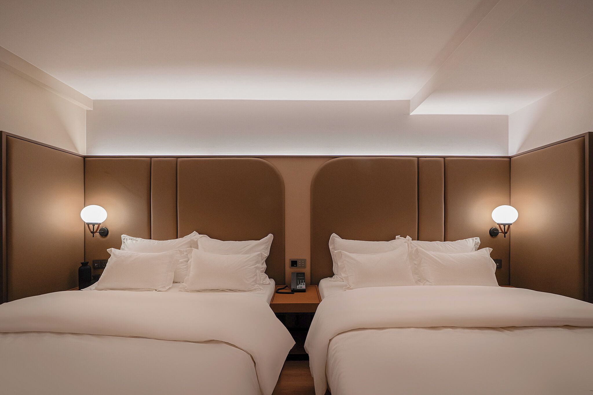Una habitación de hotel con dos camas, una mesita de noche con lámpara y un panel de control en la pared.
