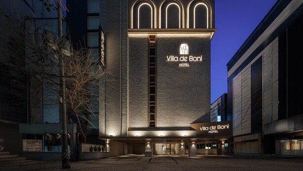 The exterior of Villa de Bani Hotel with a modern design, featuring a prominent entrance and illuminated signage. - Villa de Boni (Seoul)