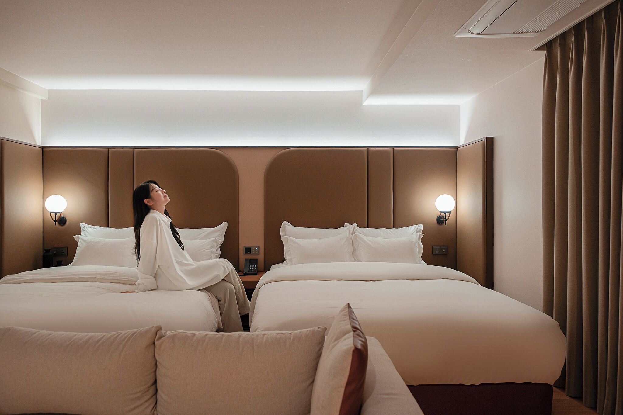 A hotel room with two beds, a headboard, bedside lamps, and a curtain.